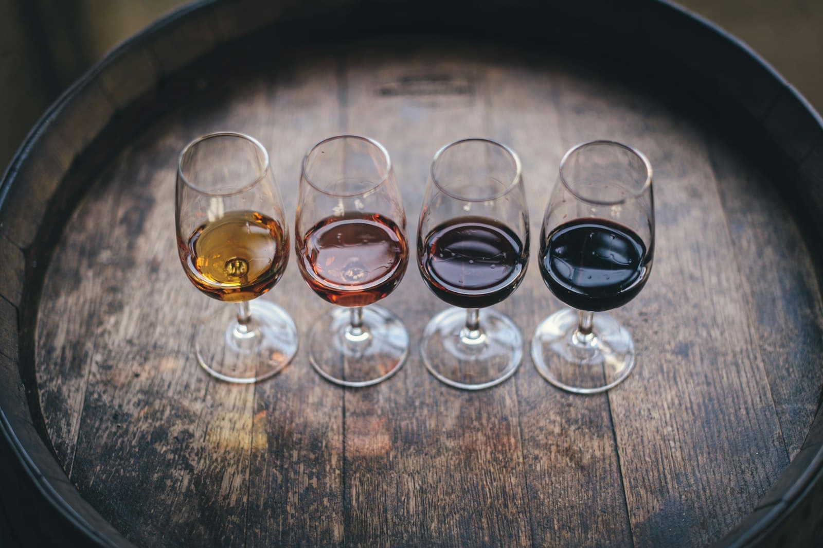 Quatre verres alignés sur une barrique, du blanc pâle au rouge profond.